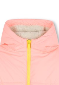 Veste à capuche rose pâle avec un col doux en beige et une fermeture éclair jaune vif au centre. Accent sur les textures de tissu et les couleurs.