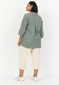 Light green long-sleeve shirt with a back pleat, paired with cream cropped pants and white sneakers with gray accents.