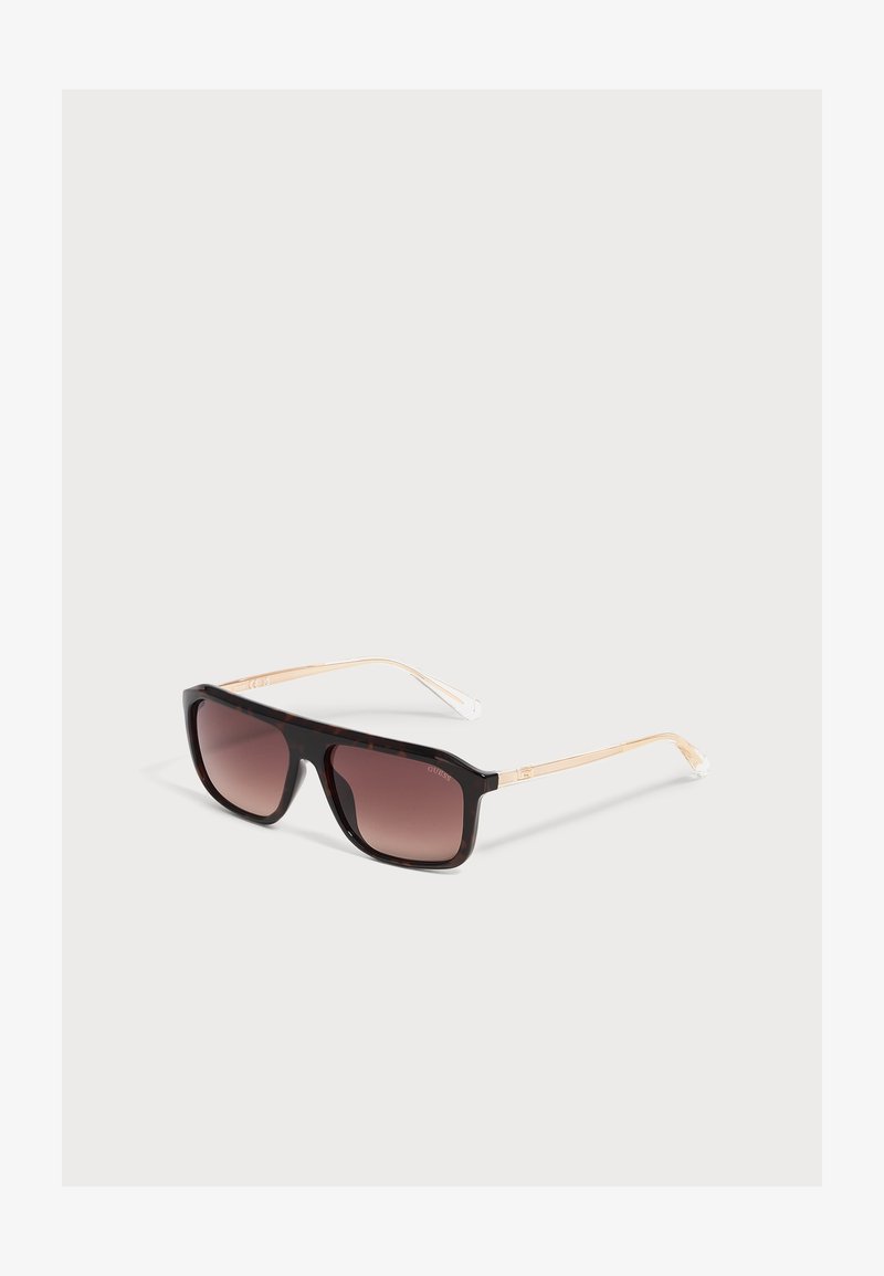 Lunettes de soleil rectangulaires avec verres dégradés brun foncé et branches fines beige clair sur fond gris clair.