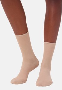 Beine mit beigen kniehohen Socken auf einem weißen Hintergrund, die die Passform und Textur der Socken zeigen.
