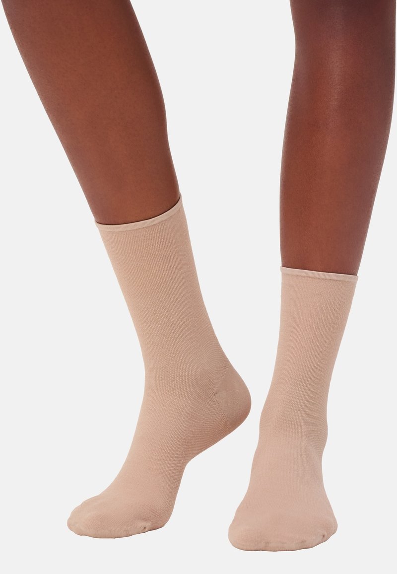 Beine mit beigen kniehohen Socken auf einem weißen Hintergrund, die die Passform und Textur der Socken zeigen.