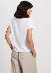 Biała koszulka z krótkim rękawem o okrągłym dekolcie i gładkiej fakturze, w połączeniu z jasnobeżowymi spodniami.