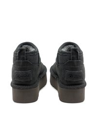 Botas de tobillo de ante negro con superficie texturizada, cuello acolchado y suela de goma que presenta una ligera plataforma y una marca en el talón.