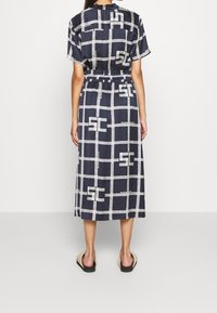 Robe midi marine à manches courtes, taille élastique et motif à carreaux crème. Présente la marque "Maison Scotch" et un design fluide.