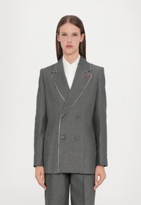 Grå dobbeltradet blazer med hvite sømmer, med store knapper og en subtil rød aksent på klaffen. Skreddersydd design med strukturerte skuldre.