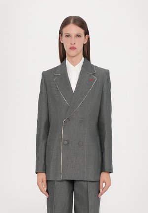Blazer grigio doppiopetto con cuciture bianche, dotato di grandi bottoni e di un sottile accento rosso sul bavero. Design sartoriale con spalle strutturate.