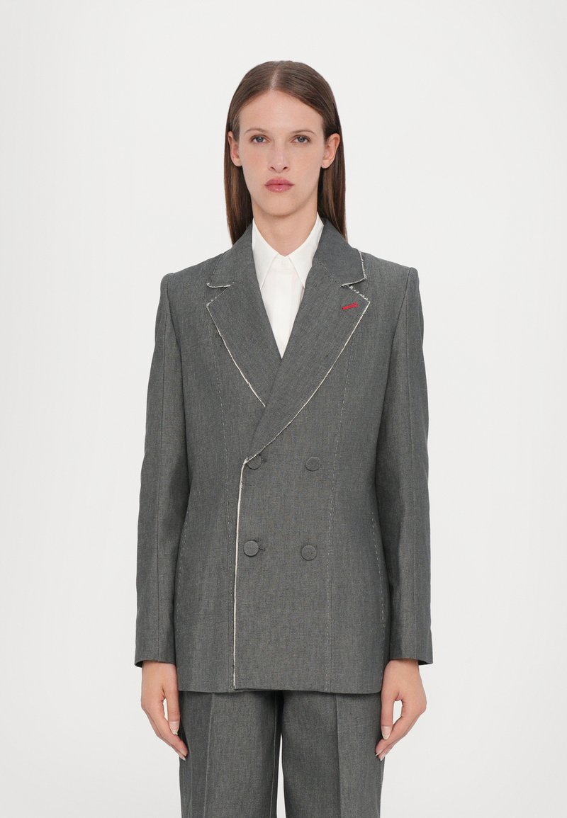 Grå dobbeltradet blazer med hvite sømmer, med store knapper og en subtil rød aksent på klaffen. Skreddersydd design med strukturerte skuldre.