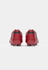 Des crampons de football rouges avec des accents noirs et des rayures argentées. Fabriqués en matériau synthétique lisse, affichant une forme aérodynamique et élégante.