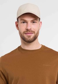 Bežna kapa s teksturiranim dizajnom, nosi se s smešnom majicom kratkih rukava boje smeđe, koja ima mali, svijetli logo na prsima.