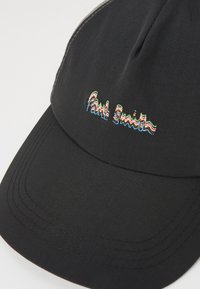 Mustaga siledast kangast müts, millel on kõver nokk. "Paul Smith" on ees mitmevärvilise niidiga brodeeritud.