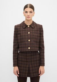 Giacca in tweed marrone con bottoni dorati, design corto e motivo scozzese. Maniche lunghe e colletto a punta. Dettaglio in tessuto texturizzato.