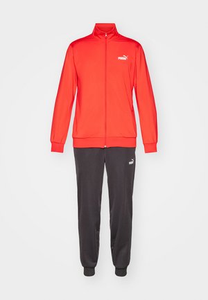 Rode trainingsjack met ritssluiting en hoge kraag, met elastische manchetten, gecombineerd met donkergrijze broek met elastische enkels, beide voorzien van een wit logo.