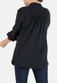 Schwarzes Langarmshirt mit lockerer Passform, Rückenfalten, umgeschlagenen Ärmeln und abgerundetem Saum. Aus weichem Stoff hergestellt, von hinten gezeigt.