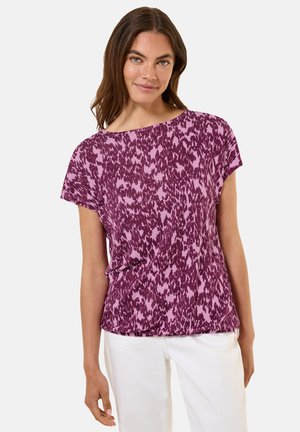 Haut à motif violet et rose avec des manches courtes, coupe décontractée et décolleté rond, en tissu doux, assorti à un pantalon blanc.