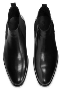 Botines de cuero negro hasta el tobillo con paneles laterales elásticos y una lengüeta en la parte posterior, con punta afilada y superficie suave y brillante.