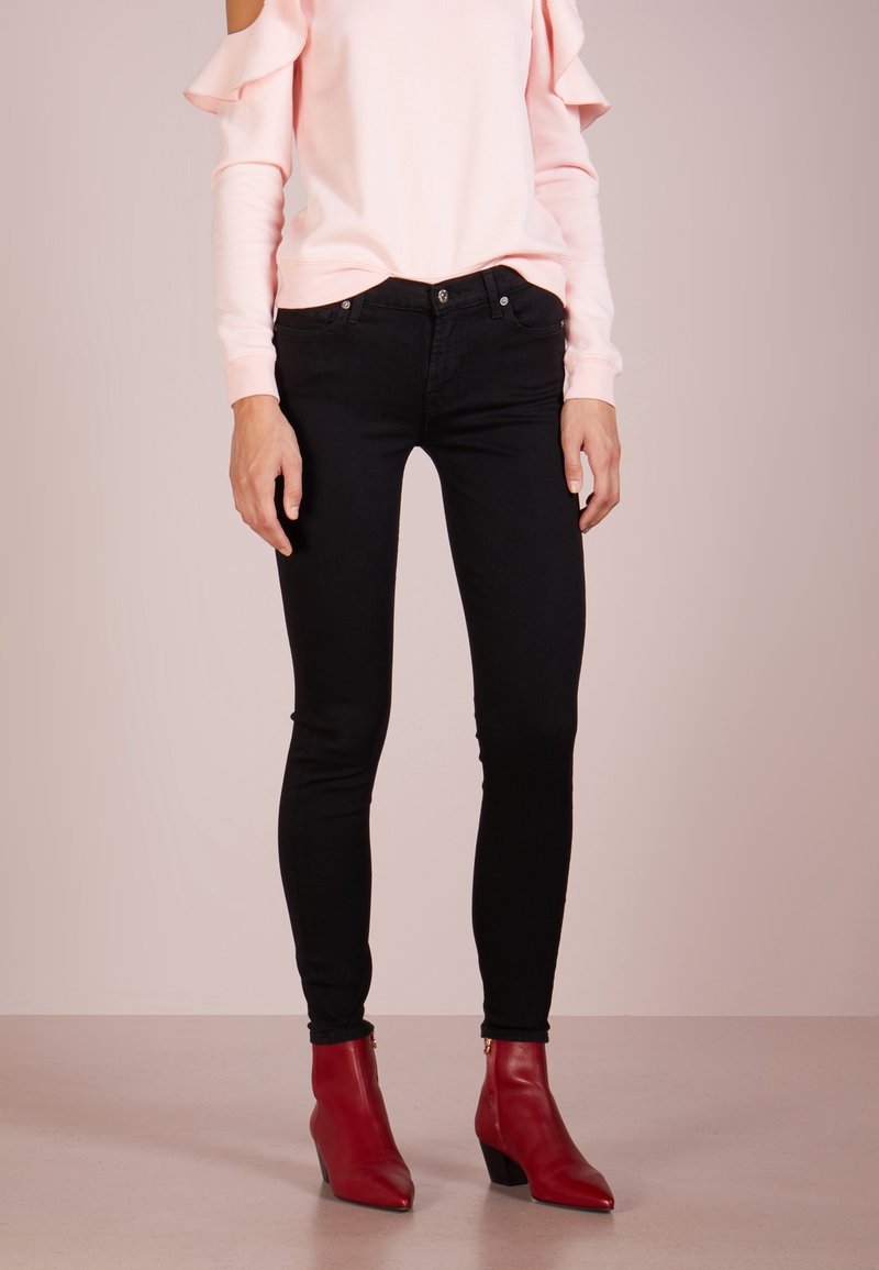 Jeans ajustados negros combinados con un suéter rosa claro con mangas con volantes, usados con botines rojos con tacón. Textura lisa y diseño entallado.