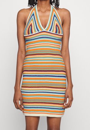 Mujer que lleva un vestido sin mangas de punto a rayas multicolor con escote en V y silueta ajustada.
