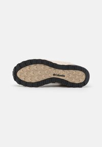 Semelle beige et noire robuste d'une chaussure Columbia avec un motif texturé pour une bonne adhérence, affichée sur un fond clair uni.