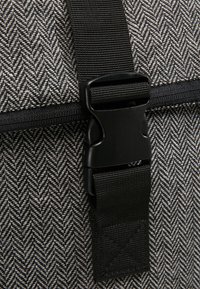 Tessuto a zigzag in grigio e bianco con una fibbia e una cinghia nere. Presenta una cerniera lungo la parte superiore per una chiusura sicura.