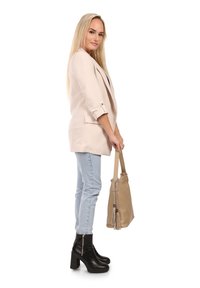 Lichtbeige blazer met opgerolde mouwen, gecombineerd met lichtblauwe jeans en zwarte plateau enkellaarsjes. Houdt een beige handtas met franjes vast.