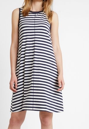 Femme portant une robe sans manches, longueur genoux, à rayures horizontales noires et blanches avec un col rond.
