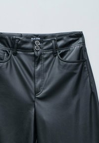 Pantalones de imitación cuero negros con doble cierre de botón plateado y bolsillos delanteros, etiquetados "Salsa Jeans" en la cinturilla.