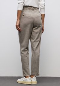 Beige, texturerade byxor med elastisk midja, två bakfickor och design med avsmalnande ben, kombinerade med vita sneakers.