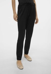 Svarta joggersbyxor i mjukt tyg, med dragsko i midjan, sidofickor och en avsmalnande design. Bärs med beige ballerinas.