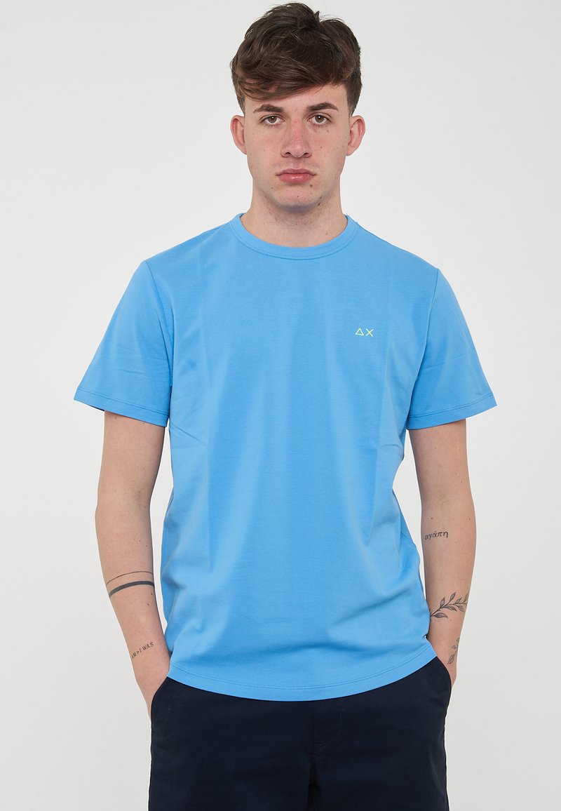 T-shirt a maniche corte, con collo tondo, in tessuto azzurro chiaro, con un piccolo logo verde sul petto e una texture liscia e morbida.