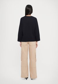 Maglione lavorato a maglia blu navy con maniche ampie abbinato a pantaloni cargo beige con tasche laterali e vestibilità morbida, visto da dietro.