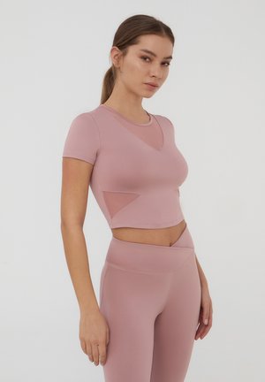Crop top sportivo rosa chiaro con maniche corte, dotato di un pannello in rete e una vestibilità aderente. Abbinato a leggings a vita alta coordinati.