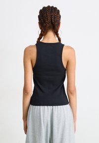 Svart ribbet tanktopp med en tettsittende design, rund halslinning og ermeløs cut, kombinert med grå joggebukser.