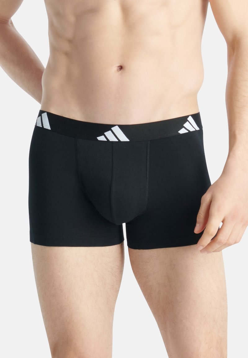 Calzoncillos boxer negros hechos de un material elástico, con una amplia cintura elástica que presenta acentos en forma de tres rayas blancas.