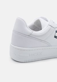 Sneaker bianco con tomaia in pelle texturizzata, colletto imbottito e suola in gomma. Presenta "TOMMY" impresso sul lato e un design con lacci.