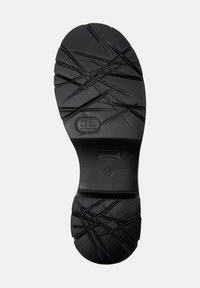Suela de zapato de goma negra con un patrón texturizado de cruces y líneas, que presenta un logo circular y la indicación de tamaño en el costado.