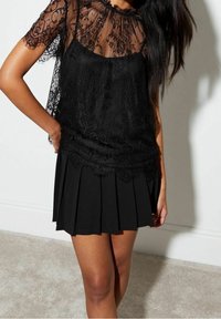 Black lace top with short sleeves over a pleated black skirt. The lace features floral patterns and a sheer neckline. Smooth fabric texture.