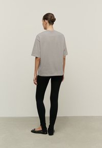 Szara, oversize koszulka z krótkim rękawem, w połączeniu z czarnymi legginsami. Gładka tekstura materiału, prosty design i brak widocznych wzorów lub dodatków.