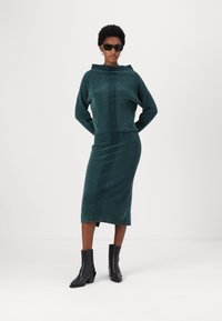 Teal gebreide trui en pencil skirt set met geribbelde accenten, voorzien van een boot neckline en een zijsplit, gecombineerd met zwarte hakken enkellaarzen.