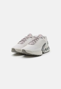 Scarpe sportive grigio chiaro con parte superiore in mesh testurizzato, chiusura con lacci e suola spessa con elementi di ammortizzazione visibili.