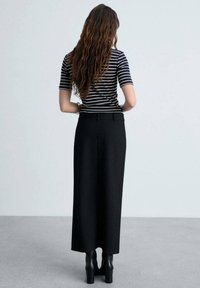 Schwarzer gerippter Maxikleid mit einer taillierten Taille, kombiniert mit einem schwarz-weißen gestreiften T-Shirt mit kurzen Ärmeln und schwarzen hohen Stiefeletten.