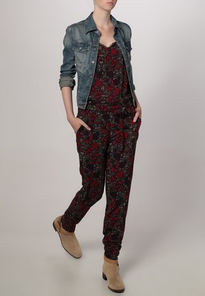 Mono floral en azul marino oscuro con patrones rojos y grises, combinado con una chaqueta de mezclilla clara. Botines de ante beige hasta el tobillo. Bolsillos en el mono.