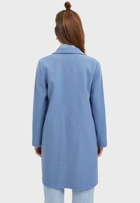 Abrigo de mezcla de lana de color azul claro con cuello con muescas, mangas largas y corte recto, que presenta una costura central en la parte posterior.