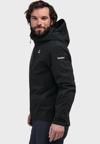Black waterproof jacket with a zip front, adjustable hood, and logo detail on the sleeve. Features a soft, smooth texture and fitted design.