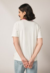 Fehér rövid ujjú póló rózsaszín gallérral, viselőn, laza szabással és puha anyagból készült, világoskék farmernadrággal párosítva.