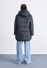 Musthave musta fliisjakker, millel on kapuuts, üleskeeratud sektsioonidega ja lõdva lõikega. Kombineeritud helesiniste laia jala teksadega.