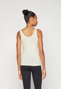 Top giallo chiaro senza maniche con scollatura rotonda e spalline sottili, realizzato in un materiale morbido, abbinato a leggings neri. Vista posteriore mostrata.