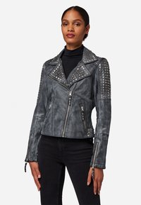 Grijze leren motorjack met metalen studs op de schouders, ritssluiting aan de voorkant en asymmetrische kraag. Heeft twee zijzakken.