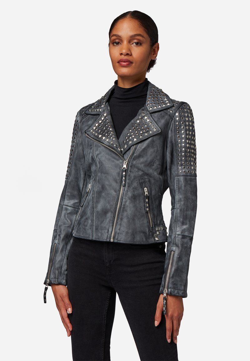 Grijze leren motorjack met metalen studs op de schouders, ritssluiting aan de voorkant en asymmetrische kraag. Heeft twee zijzakken.