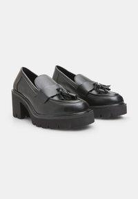Mocasini negri din piele cu toc gros, având o talpă plată, accente de ciucuri pe vârf și o textură netedă.