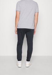 Harmaavalkoraidallinen lyhythihainen t-paita yhdistettynä mustiin kapealahkeisiin verryttelyhousuihin ja valkoisiin lenkkareihin, joissa on beigejä yksityiskohtia, nähtynä takaapäin.